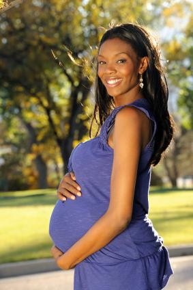 smiling pregnant woman standing outside and holding her belly