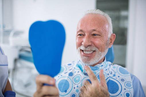 Older patient at dentist appointment looking into a and mirror and gensturing towards his face