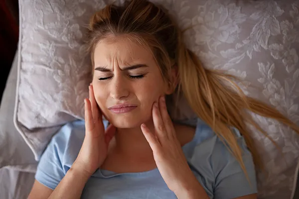 Woman in pain rubbing her jaw while in bed