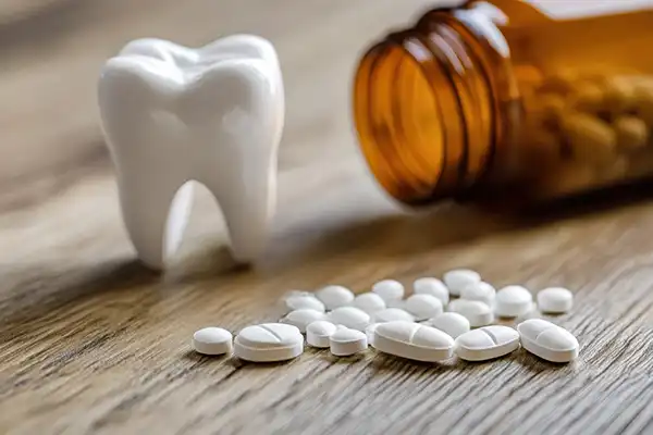 Tooth model sitting beside a small pile of pain relief pills that spilled out of a nearby bottle.
